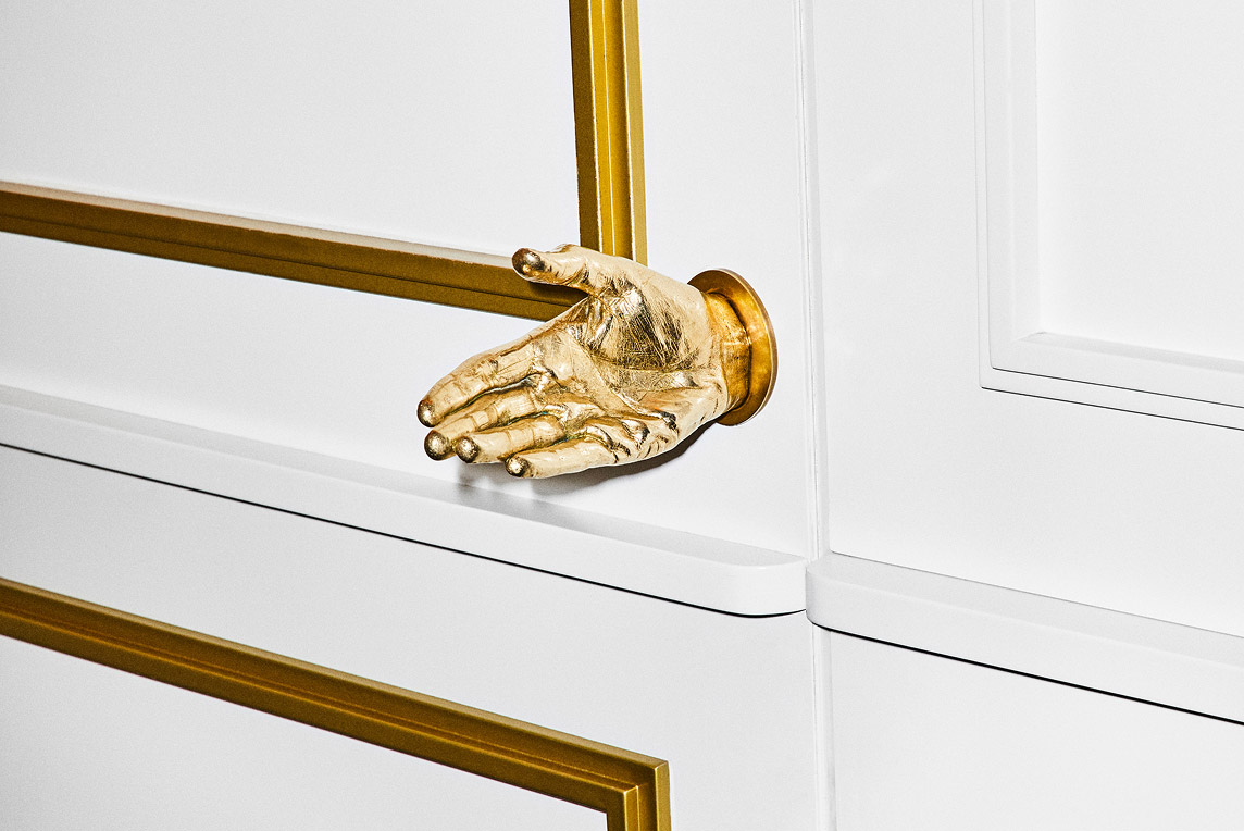 White door with gold outlines and a golden hand as the doorknob